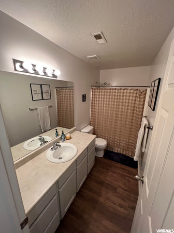 Bathroom with a textured ceiling, dark hardwood floors, mirror, and vanity