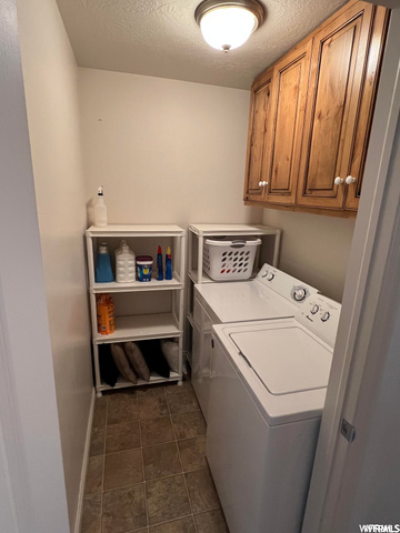 Clothes washing area with dark tile floors, a textured ceiling, and washing machine and clothes dryer