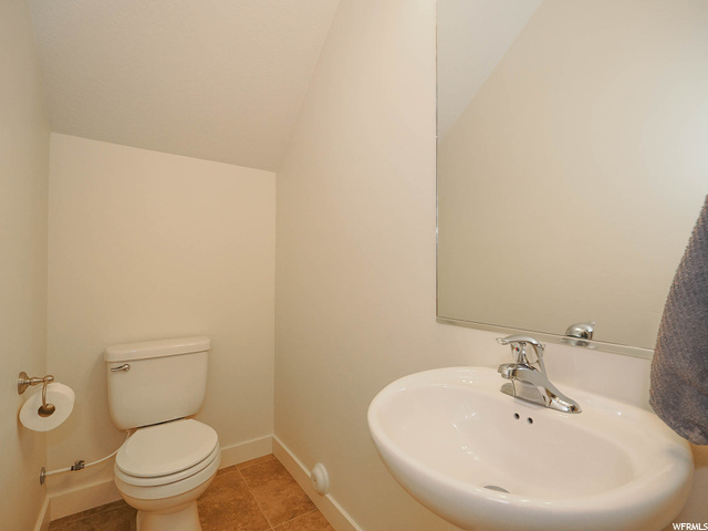 Bathroom with washbasin, light tile flooring, mirror, and lofted ceiling
