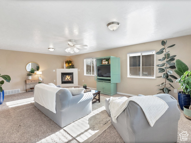 Living room with ceiling fan, light carpet, gas fireplace and natural light.