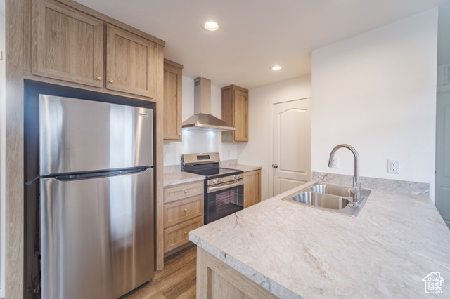 Kitchen with appliances with stainless steel finishes, light wood-type flooring, wall chimney range hood, sink, and light brown cabinets