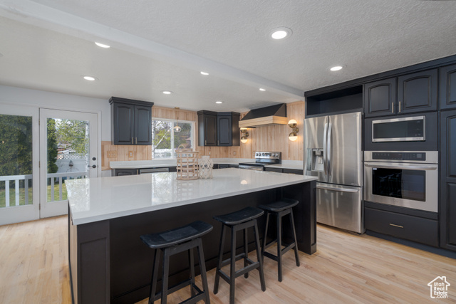 Kitchen with a center island, a kitchen bar, light hardwood floors, stainless steel appliances, and custom range hood