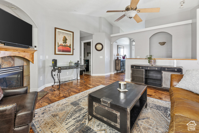 Living room featuring high vaulted ceiling, a tiled fireplace, wood-type flooring, and ceiling fan