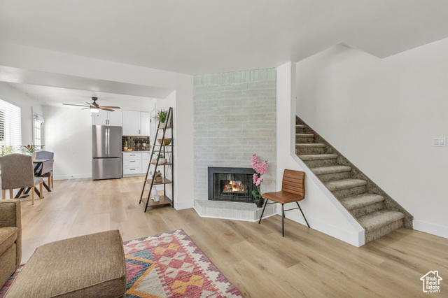 Living room with light hardwood / wood-style floors, brick wall, a brick fireplace, and ceiling fan