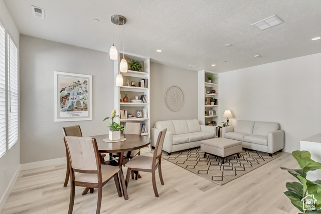 Dining space with a textured ceiling, built in shelves, and light hardwood / wood-style flooring