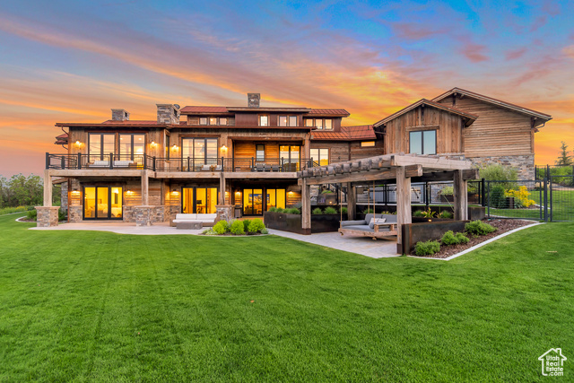 Back house at dusk with a patio area, an outdoor hangout area, a pergola, a balcony, and a yard