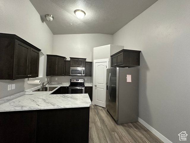 Kitchen featuring stainless steel appliances, sink, kitchen peninsula, dark brown cabinets, and laminate flooring.