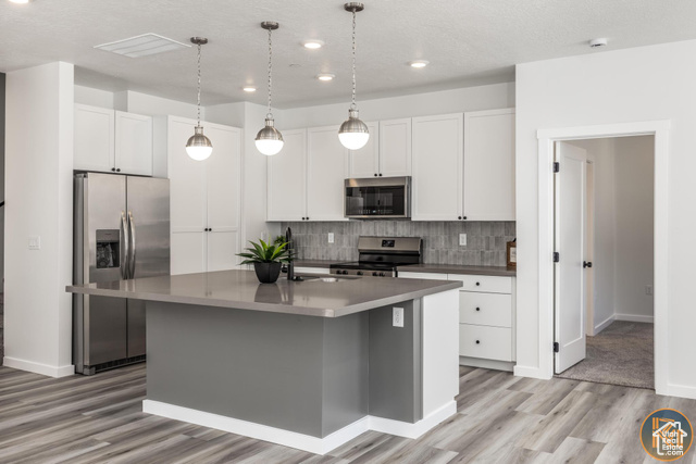 Kitchen featuring white cabinetry, decorative backsplash, light wood-type flooring, an island with sink, and appliances with stainless steel finishes