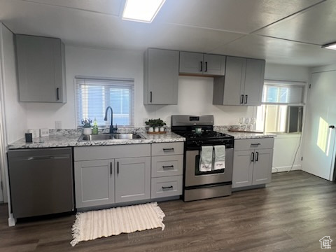 Kitchen featuring appliances with stainless steel finishes, gray cabinetry, sink, light stone counters, and dark hardwood / wood-style floors