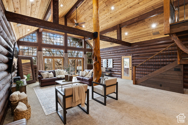 Living room with high vaulted ceiling, log walls, light colored carpet, and beam ceiling