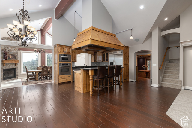 Kitchen featuring a fireplace, high vaulted ceiling, a kitchen bar, dark hardwood / wood-style floors, and appliances with stainless steel finishes