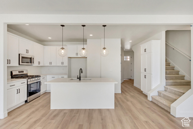 Kitchen featuring white cabinets, stainless steel appliances, a kitchen island with sink, and light hardwood / wood-style flooring