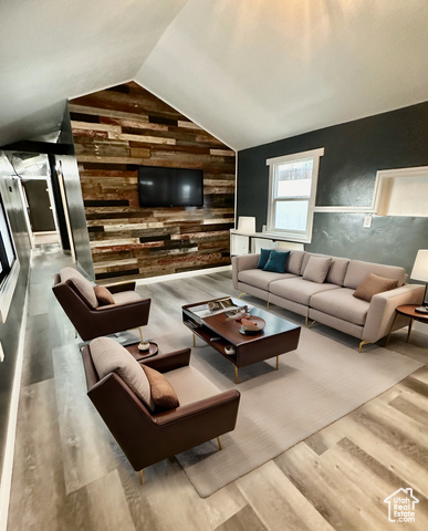 Virtually staged. Living room featuring light wood-type flooring, wooden walls, and lofted ceiling