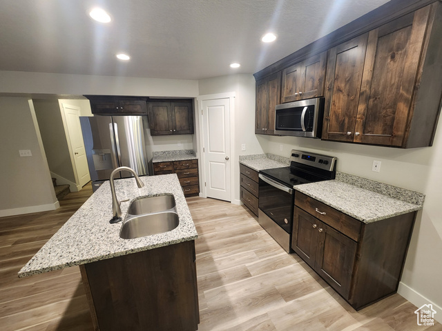 Kitchen featuring light stone countertops, appliances with stainless steel finishes, a kitchen island with sink, sink, and light hardwood / wood-style flooring