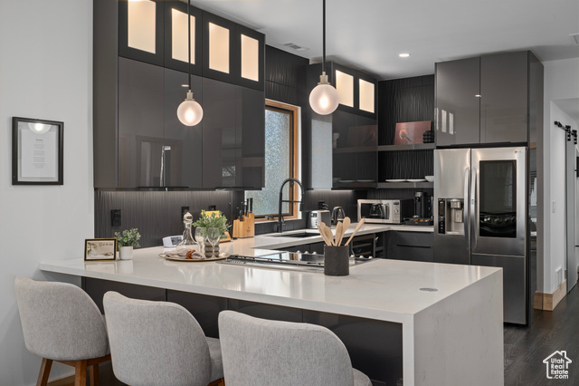 Kitchen with a kitchen breakfast bar, dark hardwood / wood-style flooring, appliances with stainless steel finishes, hanging light fixtures, and sink