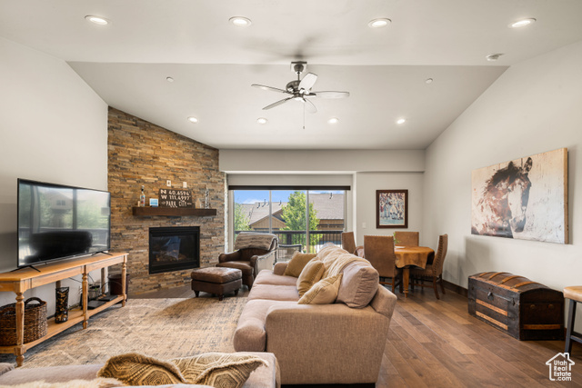 Living room with ceiling fan, vaulted ceiling, hardwood / wood-style floors, and a stone fireplace