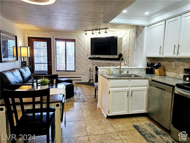 Kitchen with appliances with stainless steel finishes, ornamental molding, sink, light stone counters, and white cabinets