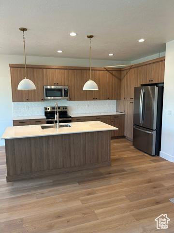 Kitchen featuring a kitchen island with sink, decorative light fixtures, appliances with stainless steel finishes, and light hardwood / wood-style floors