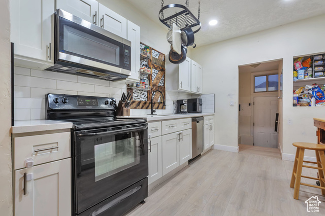 Kitchen featuring light wood-type flooring, appliances with stainless steel finishes, white cabinetry, sink, and tasteful backsplash