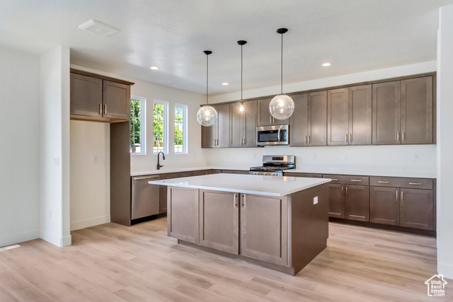 Kitchen featuring light wood-type flooring, appliances with stainless steel finishes, a center island, and hanging light fixtures