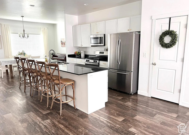 Kitchen with hanging light fixtures, white cabinetry, an island with sink, a breakfast bar, and appliances with stainless steel finishes