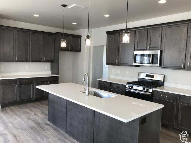 Kitchen featuring a kitchen island with sink, decorative light fixtures, sink, dark hardwood / wood-style floors, and appliances with stainless steel finishes