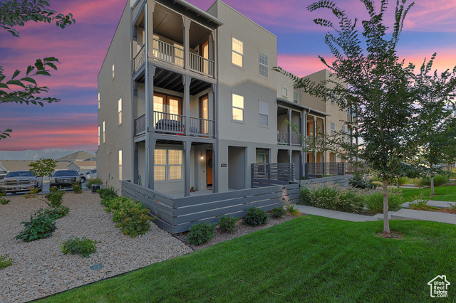 Back house at dusk featuring a balcony and a yard