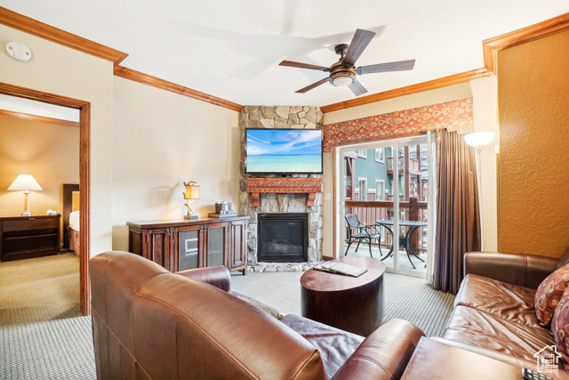 Carpeted living room with ceiling fan, crown molding, and a stone fireplace