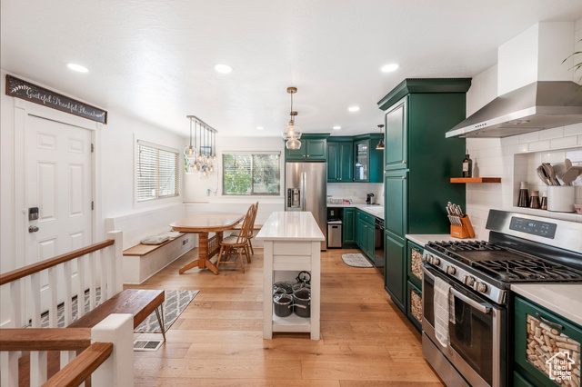 Kitchen with light wood-type flooring, wall chimney exhaust hood, stainless steel appliances, and tasteful backsplash