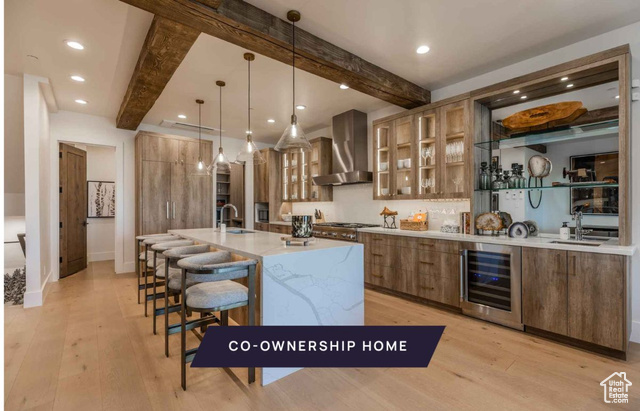 Kitchen with wine cooler, wall chimney range hood, hanging light fixtures, and beam ceiling