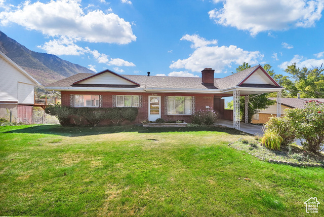 View of front facade featuring a mountain view, a front lawn, and a carport