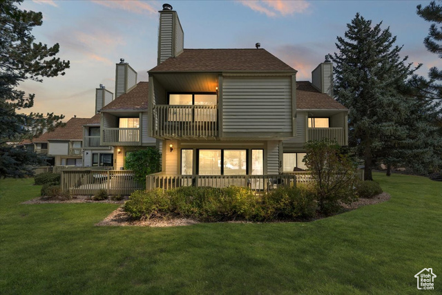 Back house at dusk with a lawn and a balcony