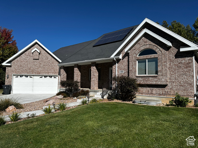 View of front facade with a garage, a porch, solar panels, and a front lawn