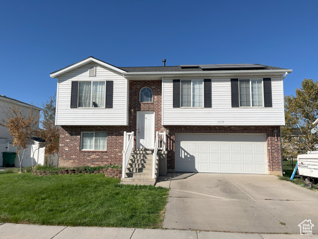 Split foyer home with a garage, a front lawn, and solar panels