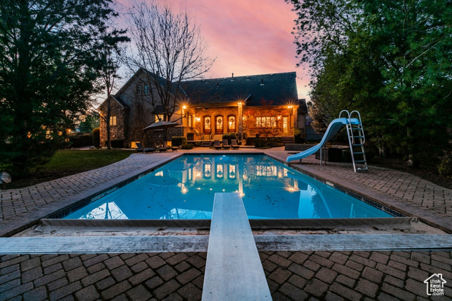 Pool at dusk with a diving board, a water slide, and a patio area