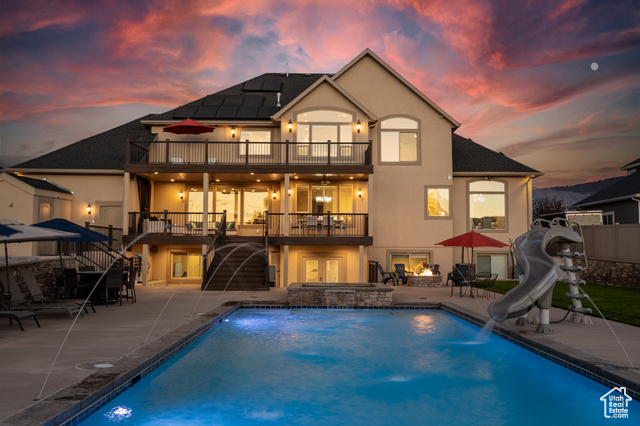 Rear view of the home highlighting the pool, slide, hot tub, fire pit, decks, & patio.