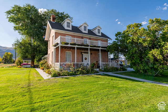 Cape cod house featuring a porch, a balcony, and a front yard