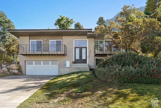 View of front of home featuring a mountain view, a front yard, a garage, and a balcony