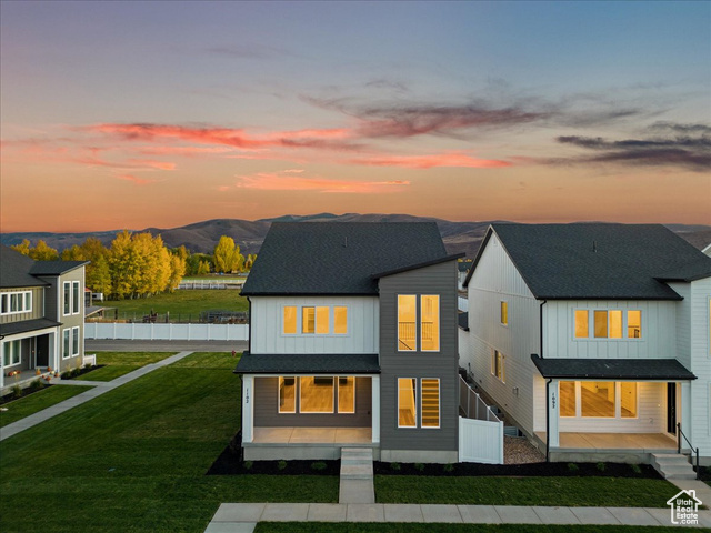 Back house at dusk featuring a mountain view and a lawn