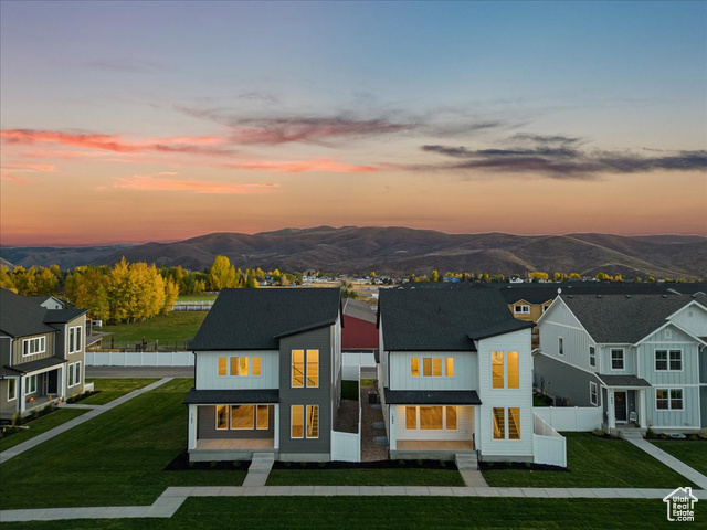 Back house at dusk featuring a mountain view and a lawn