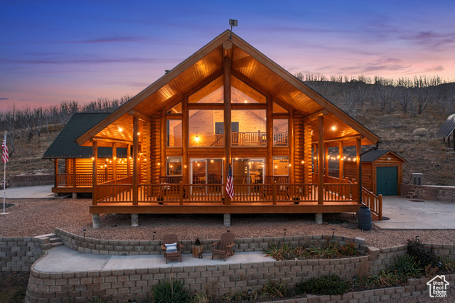 Back house at dusk featuring an outdoor structure, a garage, a deck, and a patio