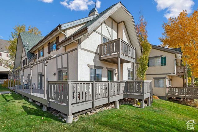 Back of property featuring a balcony, a lawn, and a wooden deck