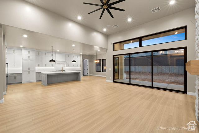 Unfurnished living room with a high ceiling, light wood-type flooring, ceiling fan, and sink