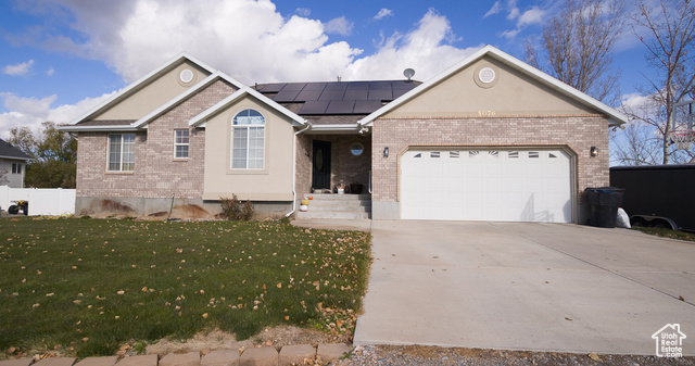 Single story home with solar panels, a garage, and a front lawn