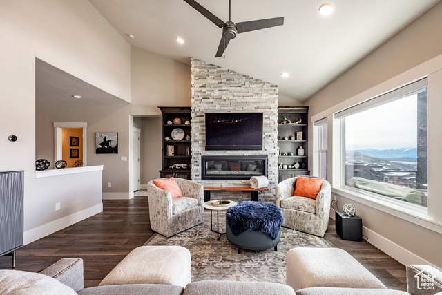 Living room with a stone fireplace, ceiling fan, high vaulted ceiling, and dark wood-type flooring