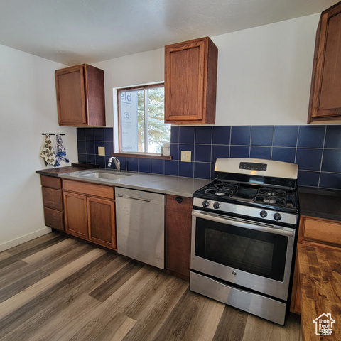 Kitchen with decorative backsplash, appliances with stainless steel finishes, dark hardwood / wood-style floors, and sink