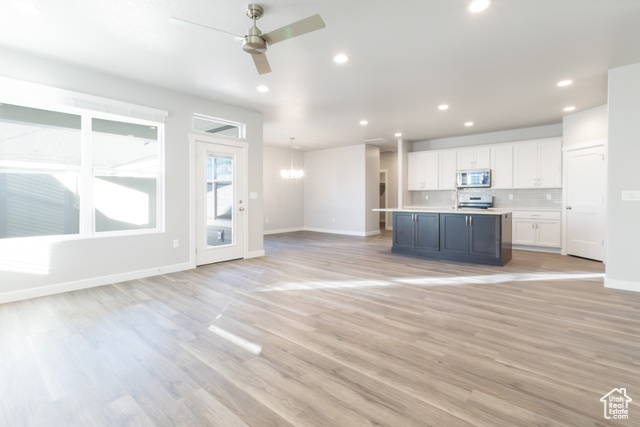 Unfurnished living room with ceiling fan with notable chandelier and light hardwood / wood-style floors