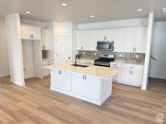 Kitchen with a kitchen island with sink, sink, white cabinets, and stainless steel appliances