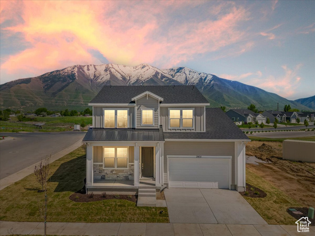 View of front of house with a mountain view, a porch, a garage, and a lawn