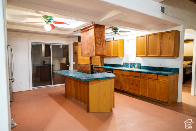 Kitchen with beam ceiling, ceiling fan, sink, stainless steel fridge, and a kitchen island